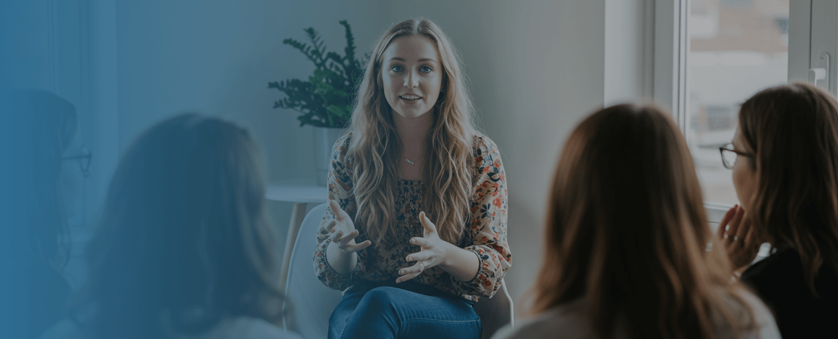 Hero (3) (1) Woman leading a group discussion or therapy session with three participants in a bright indoor setting